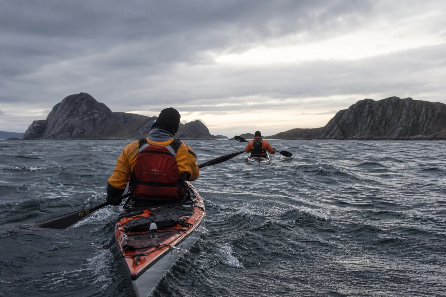 Two sea kayakers crossing rough water between rocky islands