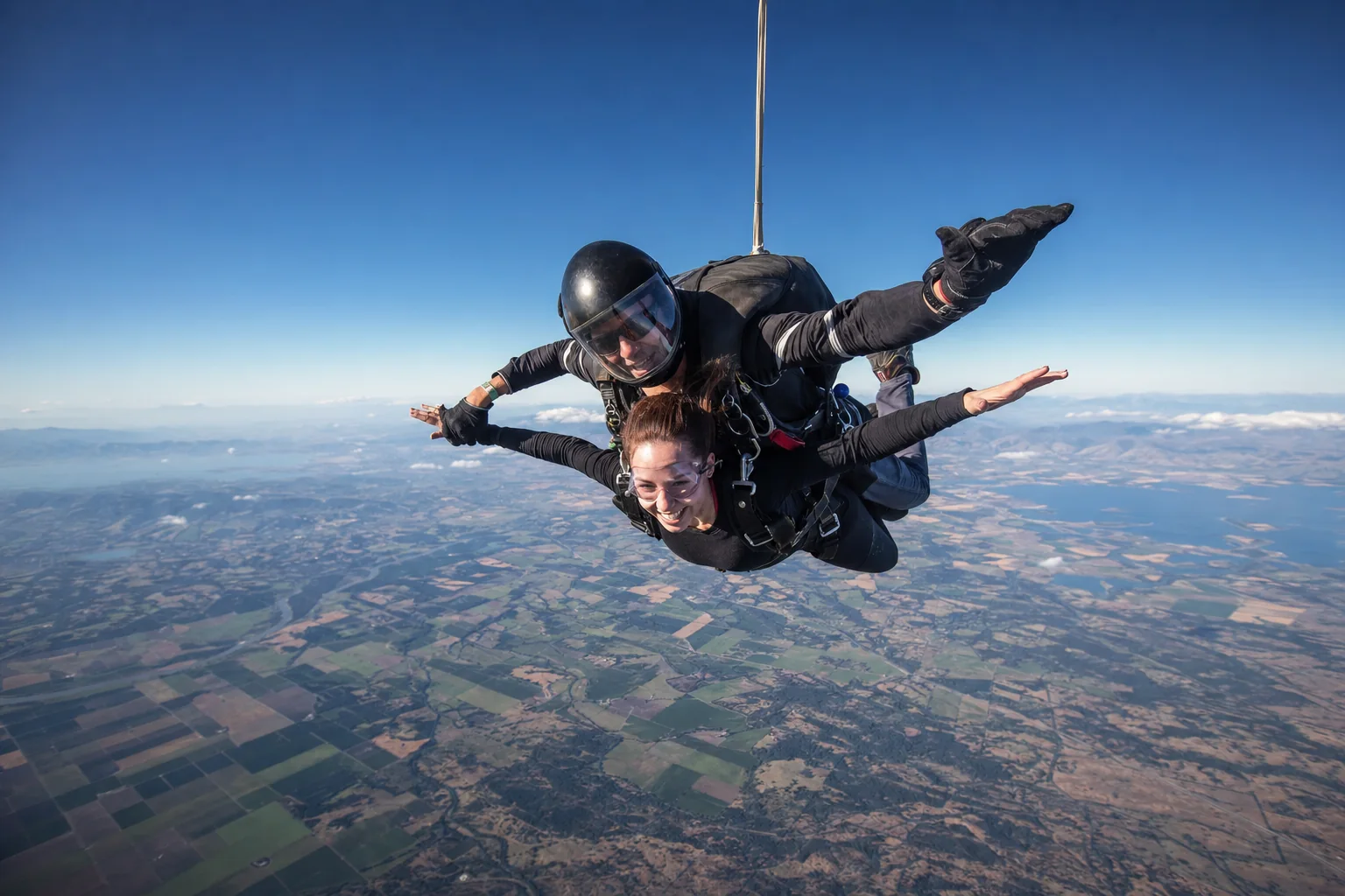 A tandem pair in stable freefall above a wide landscape